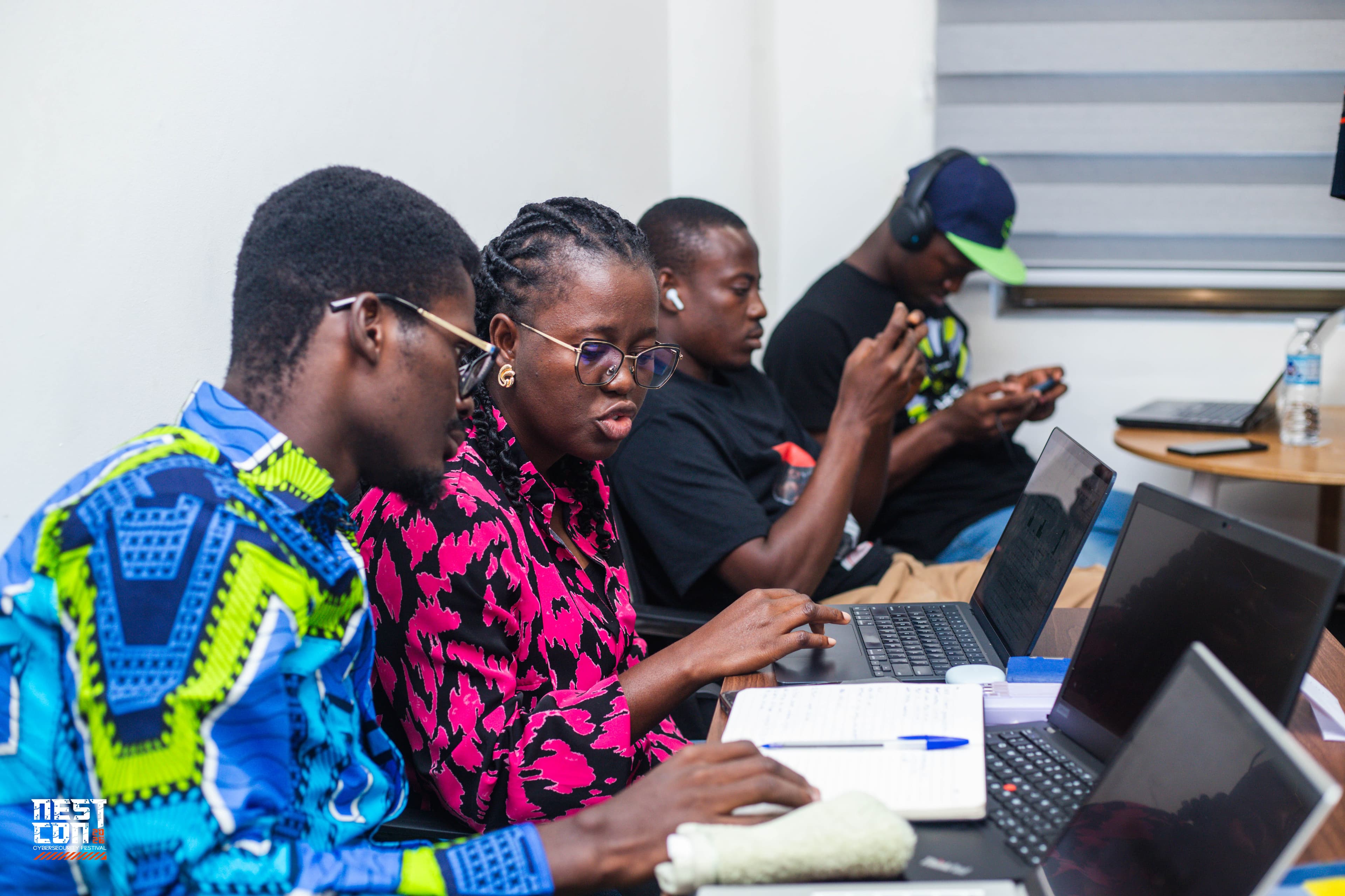 Attendees seated in a row working on laptops during a session.