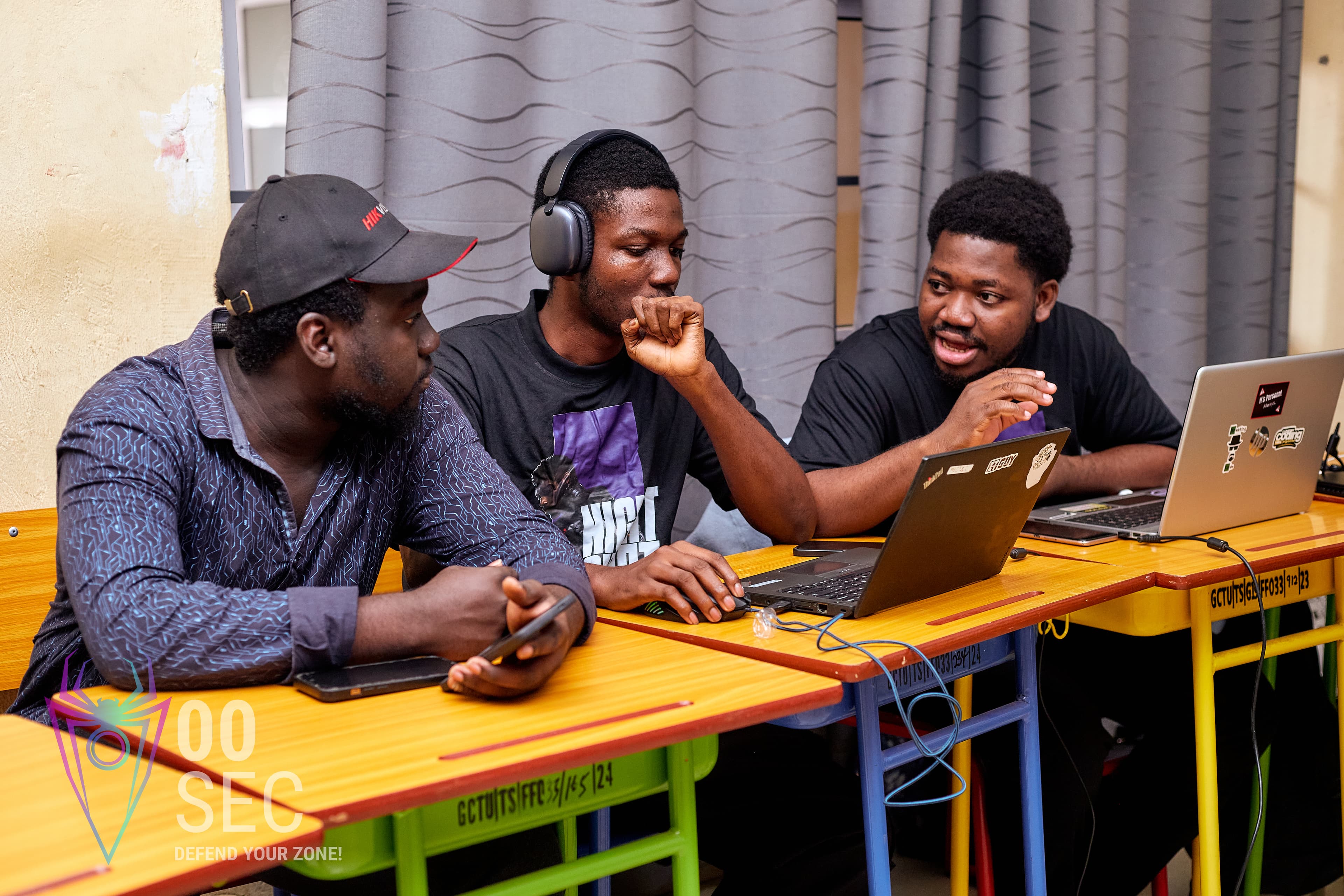Three students huddle around a laptop, deep in discussion.