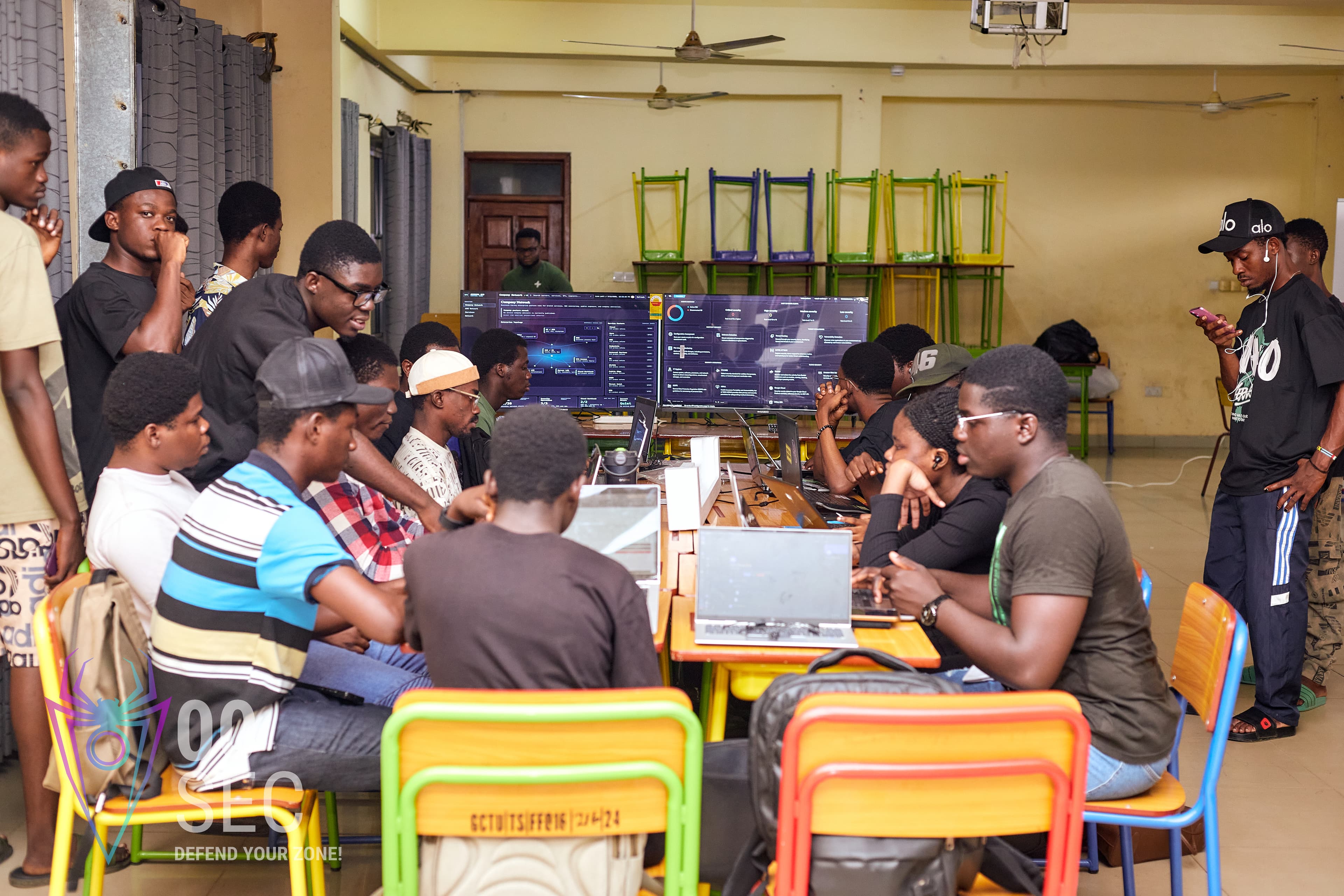 A packed room of students works together around shared screens during a cyber club activation.